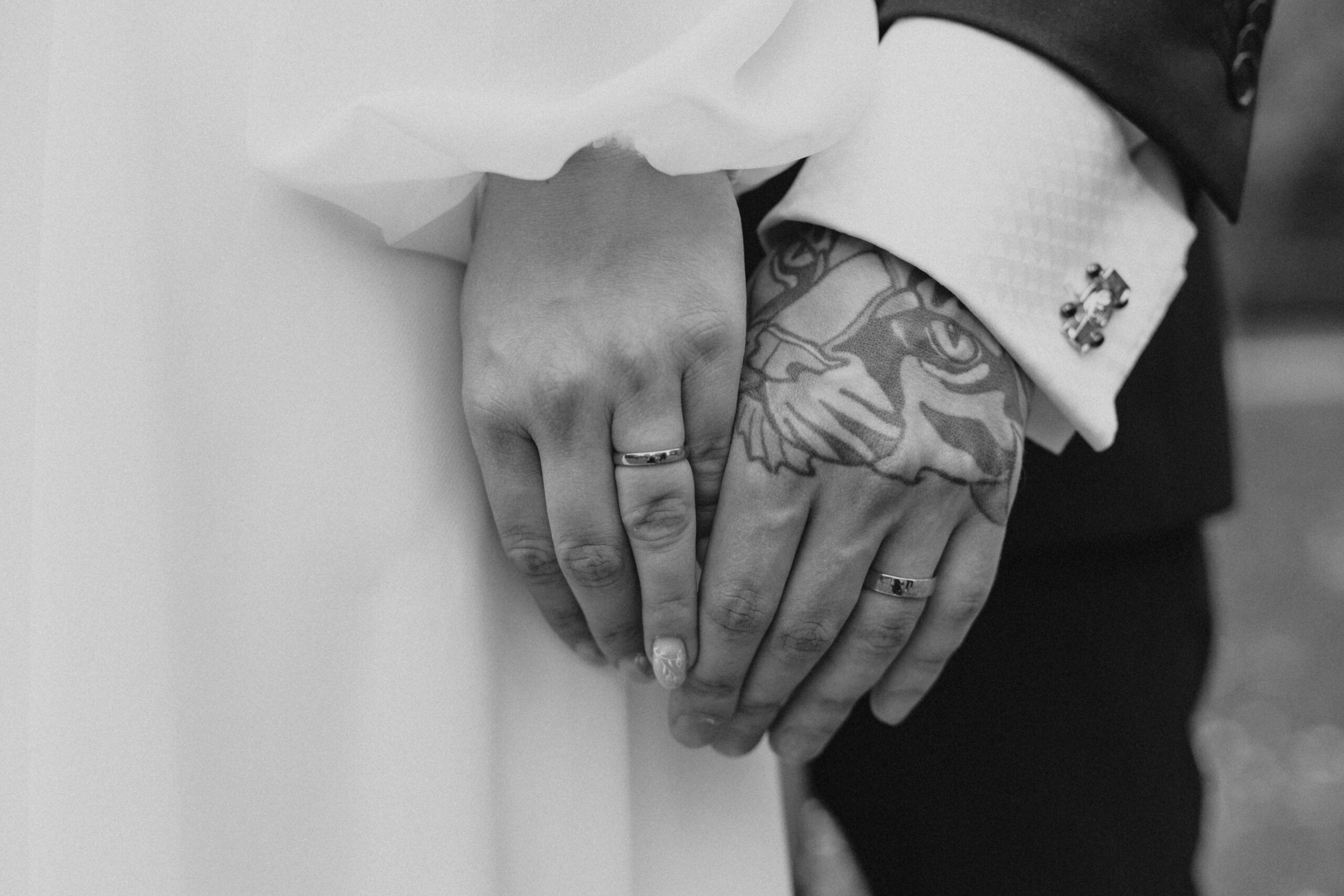 Home Close-up shot of married couple holding hands with rings, showcasing tattoos.
